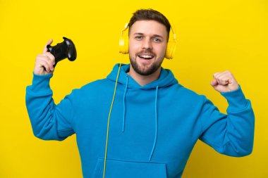 Sarı arka planda izole edilmiş bir bilgisayar oyunu kontrolörüyle oynayan beyaz bir adam güçlü bir hareket yapıyor.