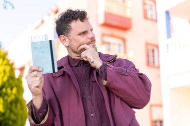 Kafkasyalı genç bir adam elinde pasaport tutarken bir fikir üretiyor ve yan bakıyor.