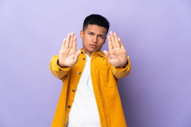 Genç Ekvadorlu adam mor arka planda izole edilmiş. Durma hareketi yapıyor ve hayal kırıklığına uğruyor.