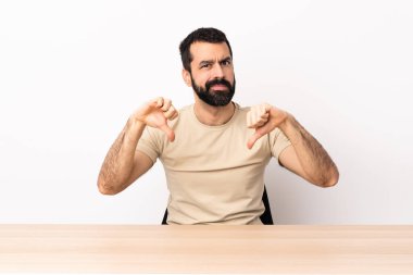 Masada sakallı, iki eliyle baş parmağını gösteren beyaz bir adam..