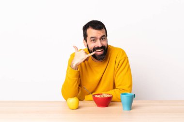 Masada kahvaltı yapan beyaz bir adam telefon jesti yapıyor. Bana geri dönüş işareti ver..