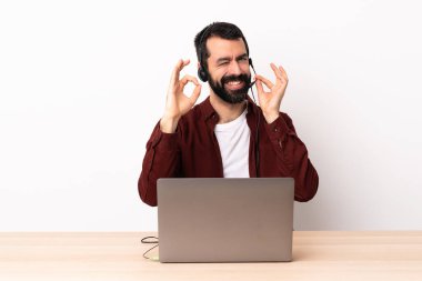 Tele pazarlamacı beyaz adam kulaklıkla çalışıyor ve dizüstü bilgisayarında parmaklarıyla işaret veriyor..