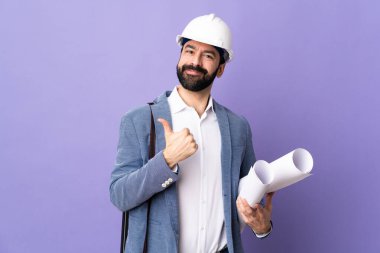 Miğferli genç mimar izole edilmiş mor arkaplanının planlarını tutuyor.