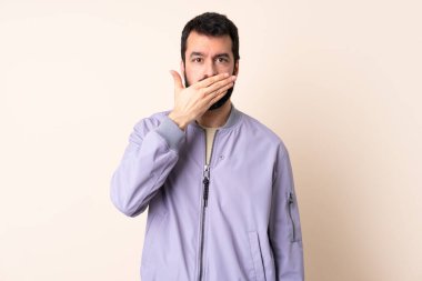 Sakallı, ceketli, izole edilmiş arka planda ağzı eliyle kapatan beyaz bir adam.