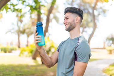 Açık havada bir şişe su ve neşeli bir ifadeyle genç yakışıklı sporcu.