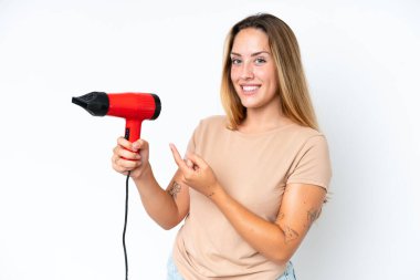 Young caucasian woman holding a hairdryer isolated on white background and pointing it