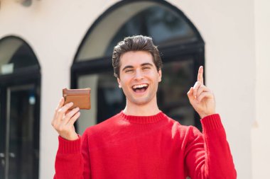 Dışarıda cüzdanını tutan yakışıklı genç adam harika bir fikri işaret ediyor.