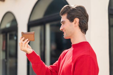Dışarıda cüzdanını tutan genç yakışıklı adam mutlu bir ifadeyle.