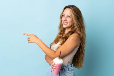 Çilekli milkshake 'i olan genç bir kadın mavi arka planda izole edilmiş.