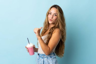 Çilekli milkshake 'i olan genç bir kadın mavi arka planda soyutlanmış gururlu ve kendinden memnun