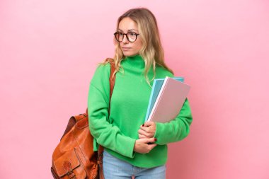 Pembe arka planda izole edilmiş genç bir bayan yan tarafa bakıyor.