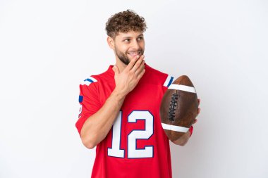 Beyaz arka planda ragbi oynayan beyaz bir adam gülümserken yukarı bakıyor.