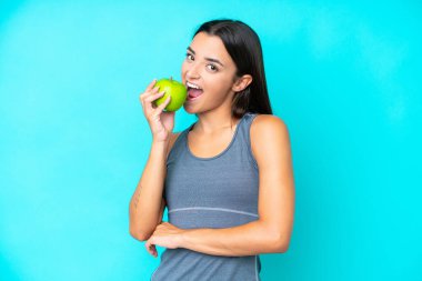 Mavi arka planda izole edilmiş beyaz bir kadın elma yiyor.