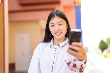 Dışarıda cep telefonu kullanan genç Çinli kadın mutlu bir ifadeyle.