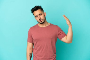 Kafkasyalı genç adam mavi arka planda izole edilmiş, yorgun ve hasta bir ifadeyle.