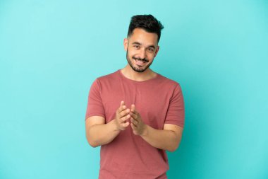 Mavi arka planda izole edilmiş genç beyaz adam bir konferansta sunumdan sonra alkışlıyor.