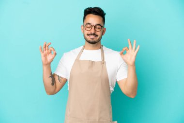 Restoran garsonu Kafkasyalı adam Zen pozunda mavi arka planda izole edilmiş.