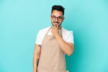Restoran garsonu beyaz adam mavi arka planda gözlüklü ve gülümsüyor.