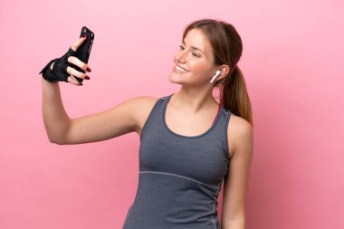 Pembe arka planda izole edilmiş genç beyaz kadın selfie çekiyor.