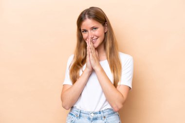 Bej arka planda izole edilmiş genç beyaz kadın avuç içlerini bir arada tutuyor. İnsan bir şey ister.