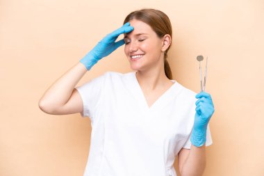 Beyaz dişçi kadın, elinde bej arka planda izole edilmiş aletlerle gülümsüyor.