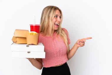 Mavi arka planda izole edilmiş yağlı yiyecekler taşıyan genç beyaz bir kadın parmak göstererek bir ürün sunuyor.