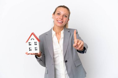 Emlakçı kadın elinde oyuncak bir ev tutuyor. Beyaz arka planda izole edilmiş. Parmağını kaldırıp kaldırıyor.