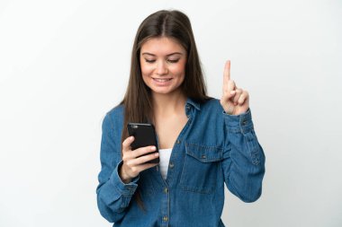 Beyaz arka planda cep telefonu kullanan ve parmağını kaldıran beyaz tenli genç bir kadın.