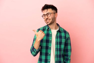 Pembe arka planda izole edilmiş genç beyaz adam bir ürünü sunmak için kenarı işaret ediyor.