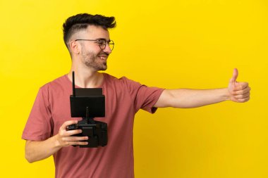 Elinde uzaktan kumandayı tutan adam sarı arka planda izole edilmiş bir şekilde baş parmak hareketi yapıyor.