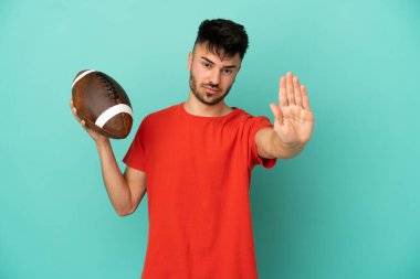 Genç beyaz adam mavi arka planda ragbi oynuyor. Durma hareketi yapıyor.