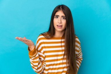 Mavi arka planda izole edilmiş genç beyaz kadın şüpheli hareketler yapıyor.