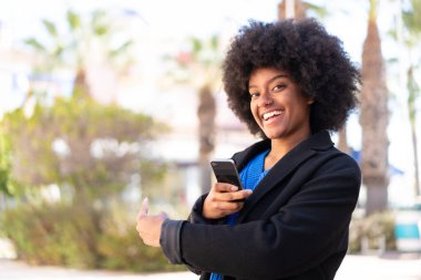 Açık havada cep telefonu kullanan Afrikalı Amerikalı bir kız.