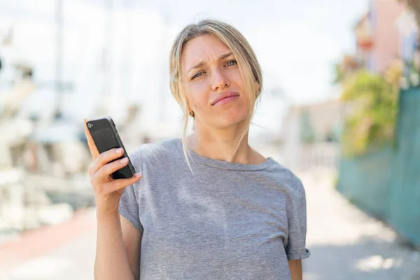 Young Blonde Woman Using Mobile Phone Outdoors Sad Expression — Stock Photo, Image