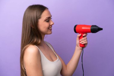 Young caucasian woman holding a hairdryer isolated on purple background with happy expression