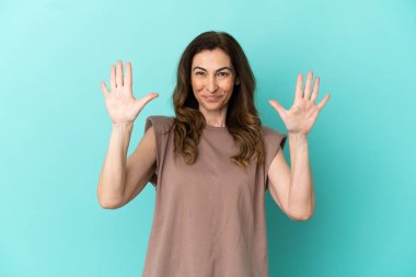 Mavi arka planda izole edilmiş orta yaşlı beyaz kadın parmaklarıyla 10 kişi sayıyor.