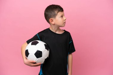 Pembe arka planda izole edilmiş beyaz futbolcu çocuk yan tarafa bakıyor.