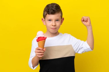 Sarı arka planda izole edilmiş kornet dondurması olan beyaz çocuk güçlü bir jest yapıyor.
