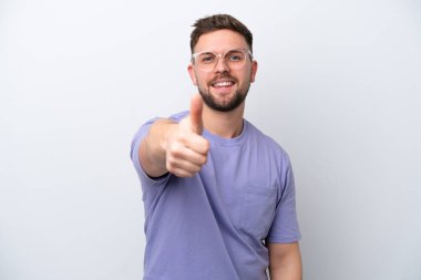 Beyaz arka planda izole edilmiş beyaz bir genç. Başparmakları havada. Çünkü iyi bir şey oldu.