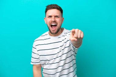 Mavi arka planda izole edilmiş genç beyaz adam hayal kırıklığına uğramış ve ön tarafı işaret ediyor.