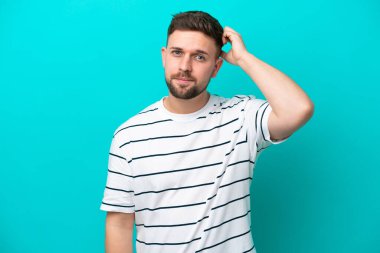 Kafkasyalı genç adam mavi arka planda izole edilmiş, hayal kırıklığı ifadesi var ve anlamıyor.