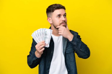 Kafkasyalı genç adam sarı arka planda izole edilmiş bir sürü para alıyor. Şüpheleri var.