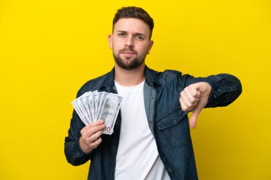 Kafkasyalı genç adam, sarı arka planda izole edilmiş bir sürü para alıyor.