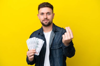 Kafkasyalı genç adam çok para alıyor. Sarı arka planda izole edilmiş. Para hareketi yapıyor.