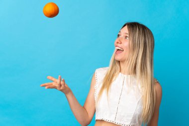 Mor arka planda izole edilmiş genç sarışın kadın elinde bir portakal tutuyor.