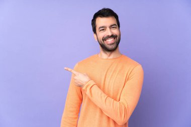 İzole edilmiş mor arka planda beyaz yakışıklı bir adam bir ürünü sunmak için yan tarafı işaret ediyor.