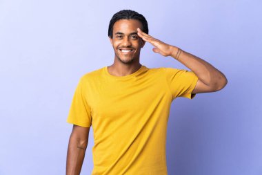 Örgülü genç Afrikalı Amerikalı adam mor arka planda izole edilmiş mutlu bir ifadeyle selamlıyor.