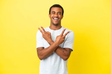 Sarı arka planda, gülümseyen ve zafer işareti gösteren Afro-Amerikalı yakışıklı bir adam.