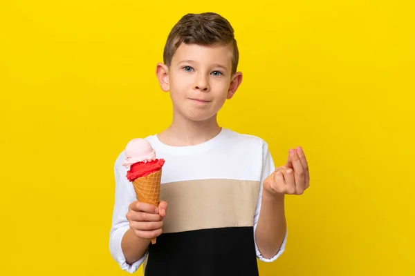 Little caucasian boy with a cornet ice cream isolated on yellow background making money gesture