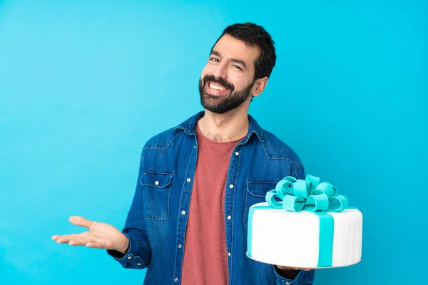 Young handsome man with a big cake over isolated blue background smiling